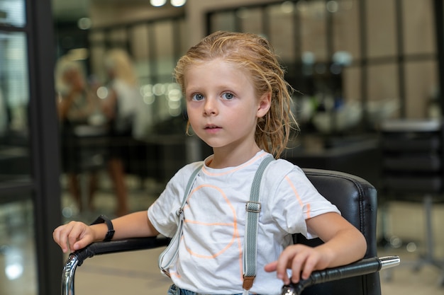 Blonder Junge mit nassen Haaren sitzt auf einem Stuhl in einem Friseurladen