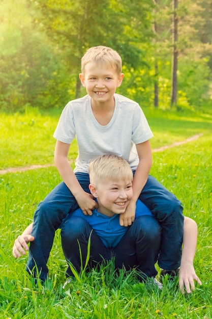 Blonder Junge sitzt auf dem Rücken eines Freundes in einem sonnigen Sommerpark