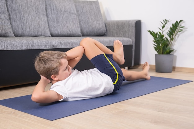 Blonder Junge treibt Sport auf Yogamatte. Körperliche Aktivität des Kindes. Sport gesunder Lebensstil aktive Freizeit zu Hause während der COVID-19-Quarantäne.