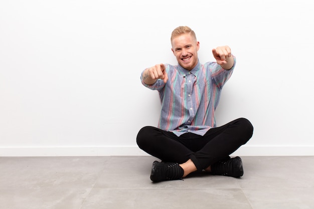 blonder junger Mann sitzt und zeigt auf