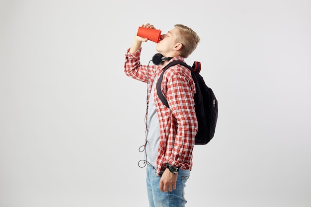 blonder Kerl, mit Rucksack trinkt aus dem roten Plastikbecher