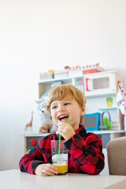 Blonder Kleinkindjunge in seinem Spielzimmer, der Saft trinkt