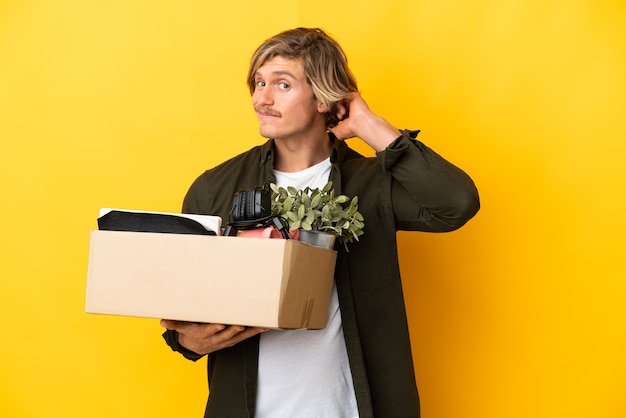 Blonder Mann, der eine Bewegung macht, während er eine Schachtel voller Dinge aufhebt, die auf Gelb isoliert sind und Zweifel haben