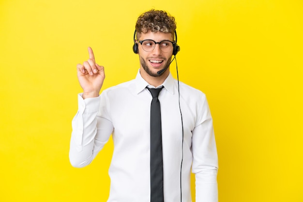 Blonder Mann des Telemarketers, der mit einem auf gelbem Hintergrund isolierten Headset arbeitet und beabsichtigt, die Lösung zu realisieren, während er einen Finger nach oben hebt