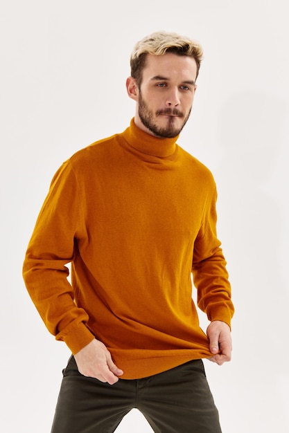 Blonder Mann in orangefarbenem Pullover auf hellem Hintergrund und dunkler Hose, ausgeschnittene Ansicht