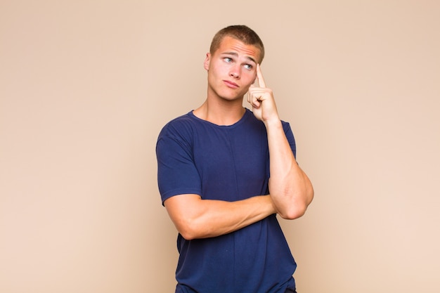 Blonder Mann mit einem konzentrierten Blick, der sich mit einem zweifelhaften Ausdruck wundert und aufschaut und zur Seite schaut