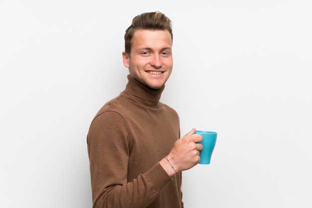 Blonder Mann über der lokalisierten weißen Wand, die einen heißen Tasse Kaffee hält