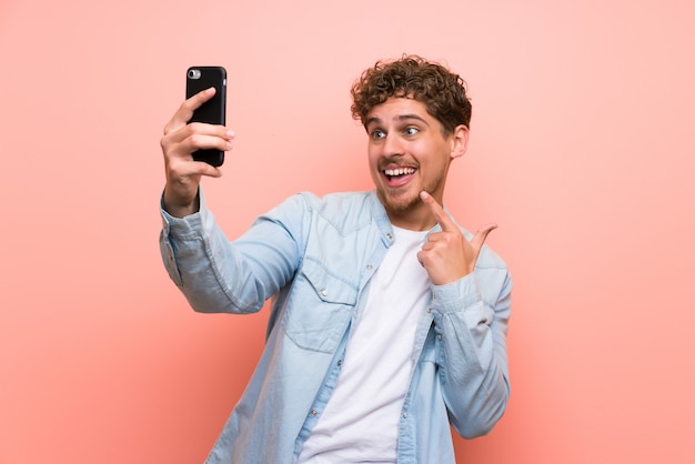 Blonder Mann über der rosa Wand, die ein selfie macht