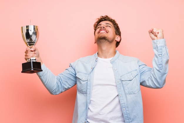 Blonder Mann über der rosa Wand, die eine Trophäe hält