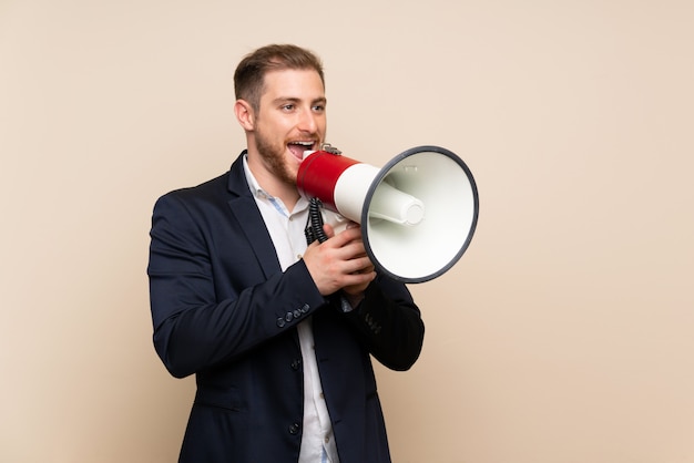 Blonder Mann über getrenntem Hintergrund schreiend durch ein Megaphon