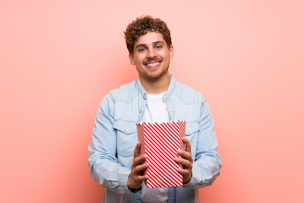 Blonder Mann über rosa Wand Popcorn essend