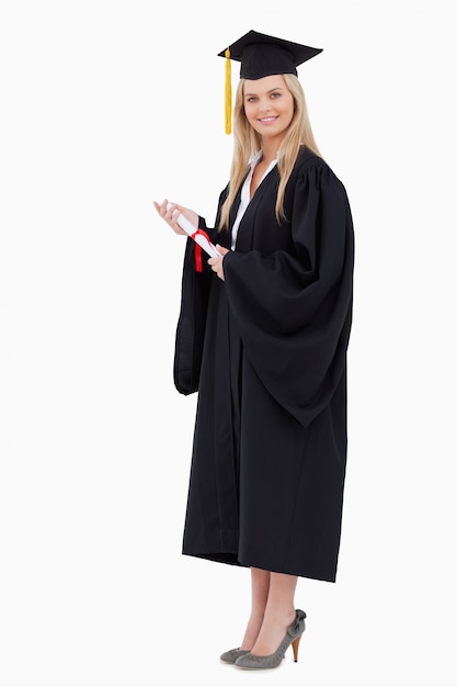 Blonder Student in der graduierten Robe, die ein Diplom hält