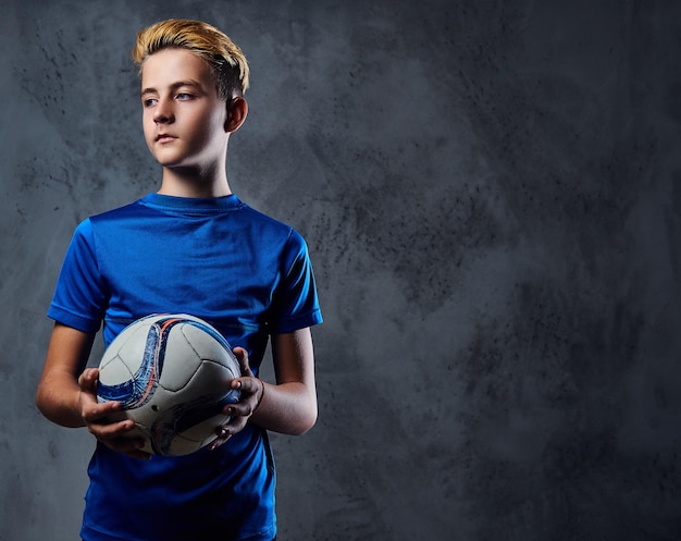 Blonder Teenager, Fußballspieler in blauer Uniform hält einen Ball.