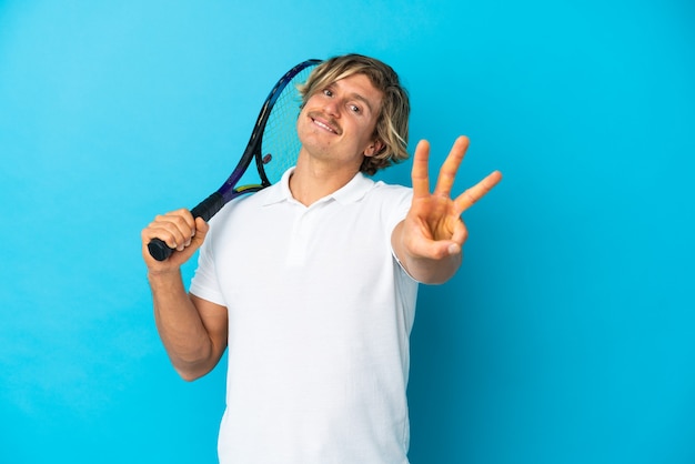Blonder Tennisspielermann lokalisiert auf blauer Wand glücklich und zählt drei mit den Fingern