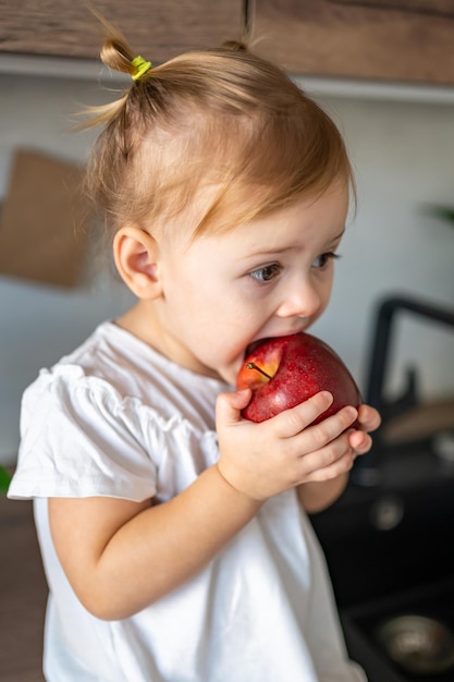 Blondes Baby, das einen Apfel im Küchenkonzept der gesunden Nahrung für Kinder isst