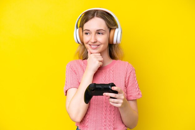 Blondes englisches junges Mädchen, das mit einem Videospielcontroller spielt, isoliert auf gelbem Hintergrund