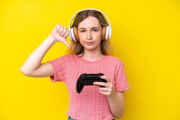 Blondes englisches junges Mädchen, das mit einem Videospielcontroller spielt, isoliert auf gelbem Hintergrund