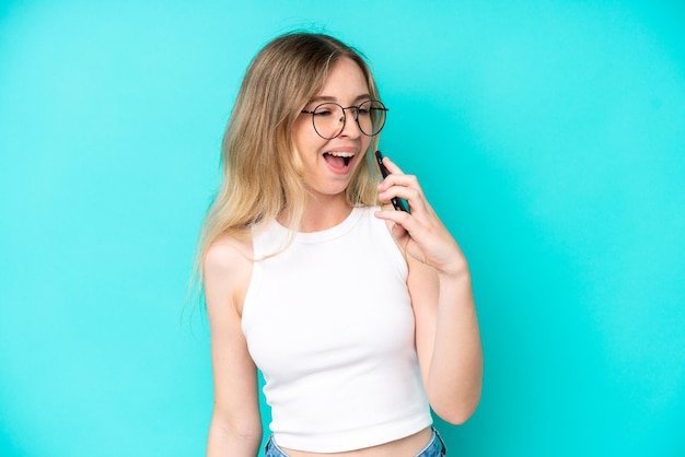 Blondes englisches junges Mädchen lokalisiert auf blauem Hintergrund unter Verwendung des Handys und des Singens