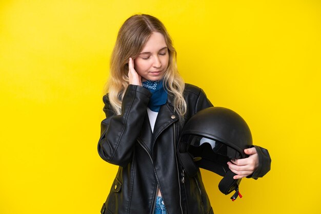 Blondes englisches junges Mädchen mit einem Motorradhelm lokalisiert auf gelbem Hintergrund mit Kopfschmerzen