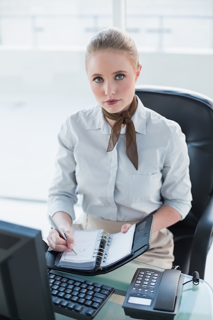 Blondes ernstes Geschäftsfrauschreiben im Tagebuch