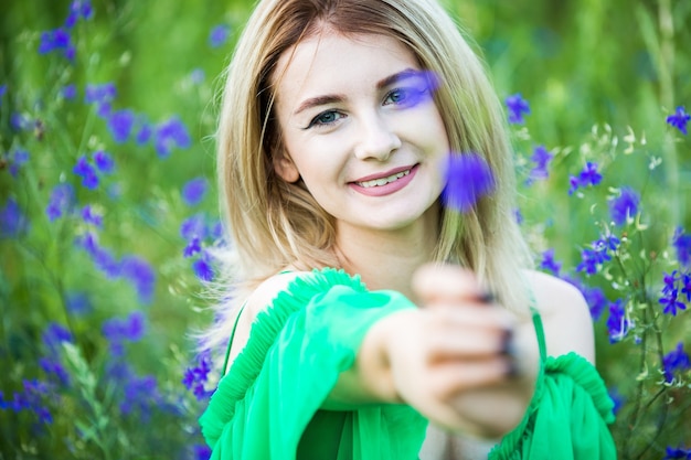 Blondes europäisches Mädchen in einem grünen Kleid auf Natur mit blauen Blumen