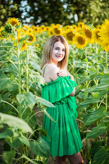 Blondes europäisches Mädchen in einem grünen Kleid auf Natur mit Sonnenblumen
