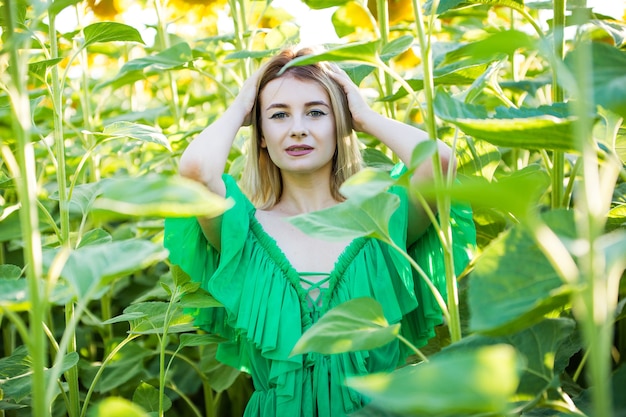 Blondes europäisches Mädchen in einem grünen Kleid auf Natur mit Sonnenblumen