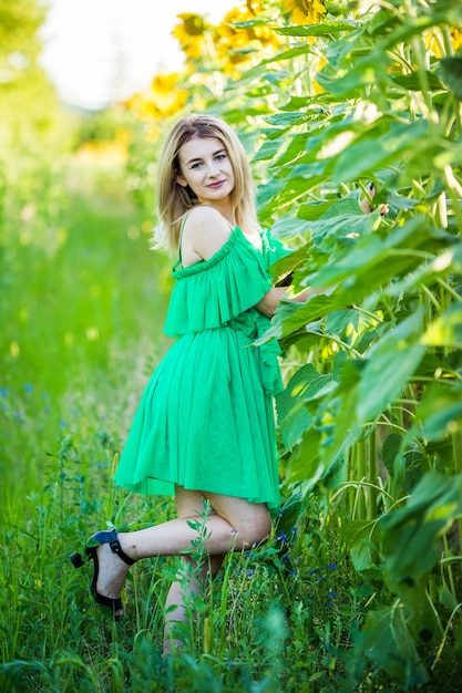 Blondes europäisches Mädchen in einem grünen Kleid auf Natur mit Sonnenblumen