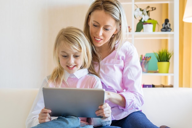 Blondes, fröhliches Mädchen mit ihrer Mutter, die zusammen einen Tablet-Computer verwendet