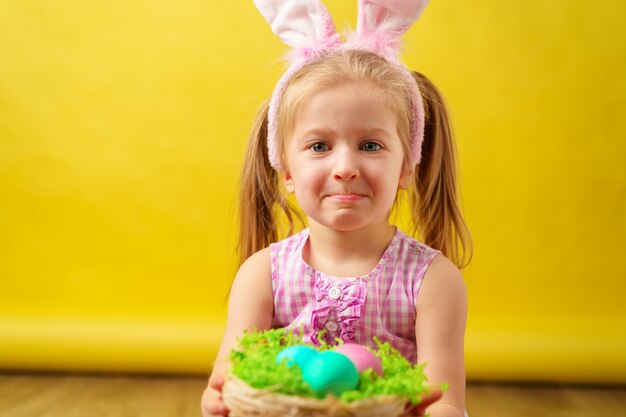 Blondes glückliches Mädchen mit Hasenohren und Korb von Eiern für Ostern