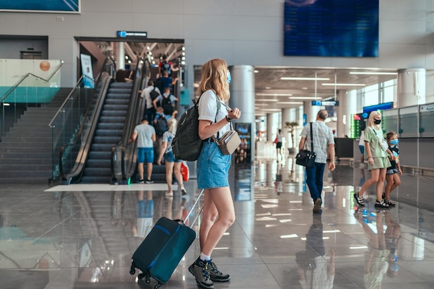 Blondes Haar, weibliche Touristenhand, die Reisepass mit Koffergepäck-Wartebereich des Flughafenterminals für eine Reise hält. Reisen nach der Covid-19-Pandemie