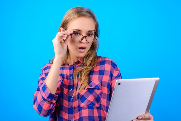 Blondes Haarmädchen, das Gläser berührt Tablette auf lokalisiertem blauem Hintergrund