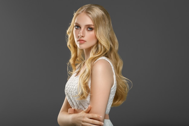 Blondes junges Modell des lockigen langen Haares. Schönheitsmädchen mit lockiger perfekter Frisur. Studioaufnahme.