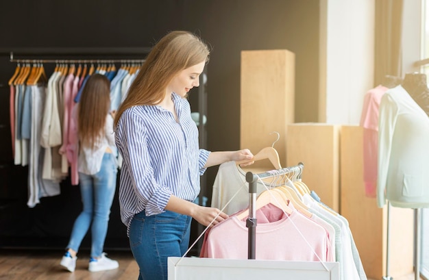 Blondes kaukasisches Mädchen, das neuen Pullover im Ausstellungsraum auswählt, freier Speicherplatz