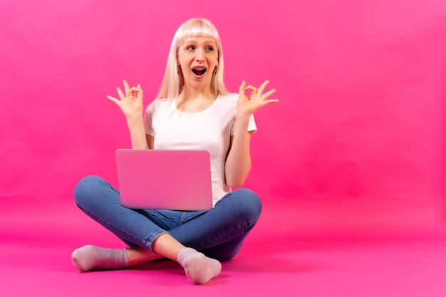 Blondes kaukasisches Mädchen mit einem Computerstudio, das auf rosafarbenem Hintergrund gedreht wurde, kopieren Sie Platz ok Geste