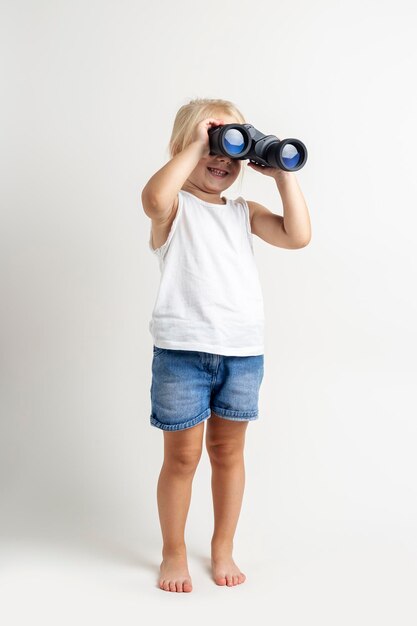 Blondes Kind, das durch ein Fernglas auf hellem Hintergrund im Studio schaut