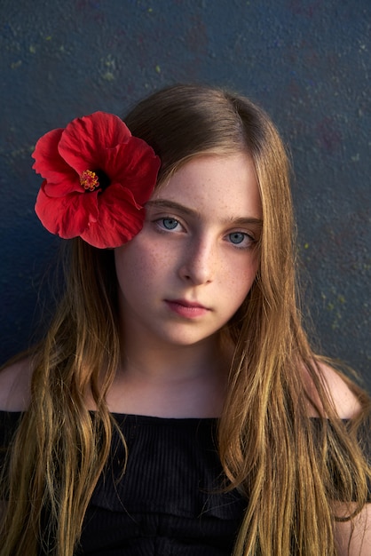 Blondes Kindermädchenporträt mit roter Blume im Haar