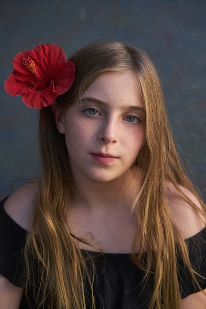 Blondes Kindermädchenporträt mit roter Blume im Haar