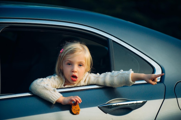 Blondes kleines Mädchen schaut aus dem Fenster im Auto und etwas zeigt eine Hand, die zeigt