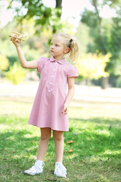 Blondes kleines Mädchen spielt mit Holzflugzeug im Park