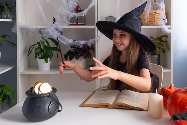 Blondes Mädchen 7-8 Jahre im Hexenkostüm feiert Halloween mit Hexenbuch und Goldschatzbonbons