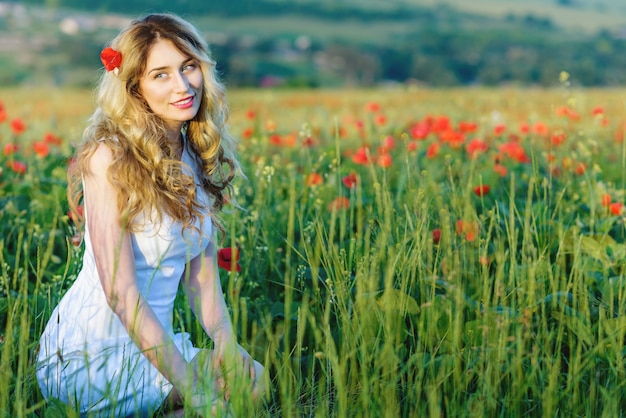 Blondes Mädchen auf dem Mohnblumengebiet, lächelnd in der Wiese der Natur