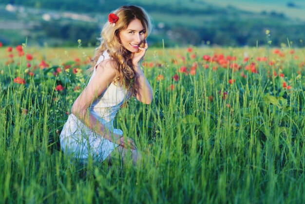 Blondes Mädchen auf dem Mohnblumengebiet, lächelnd in der Wiese der Natur