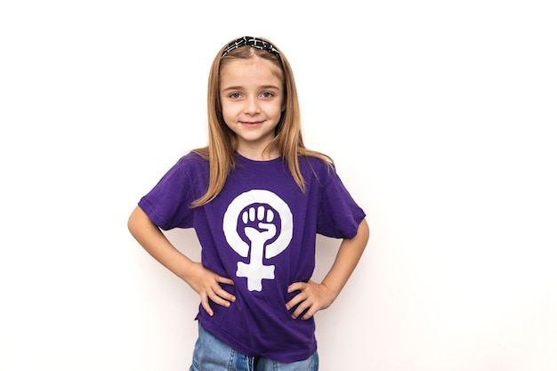 Blondes Mädchen, das ein lila T-Shirt mit dem Symbol des internationalen feministischen arbeitenden Frauentages auf einer weißen Wand trägt