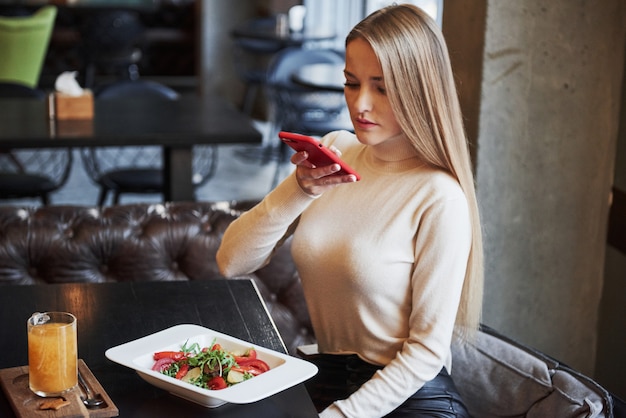 Blondes Mädchen, das Gemüsesalat im Restaurant fotografiert