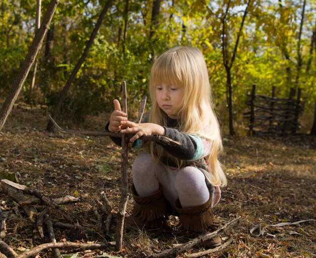 Blondes Mädchen, das sich im Herbst im Freien beim Aufbau einer Stockstruktur konzentriert