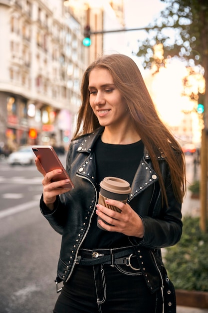 Blondes Mädchen, das Telefon mit einem Kaffee betrachtet