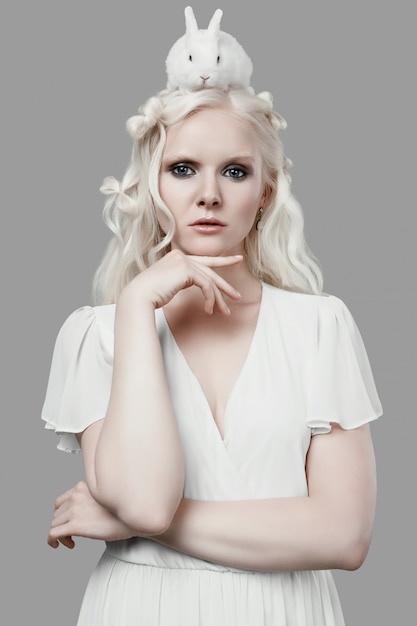Blondes Mädchen des Albinos im eleganten Kleid, das mit nettem kleinem Kaninchen aufwirft