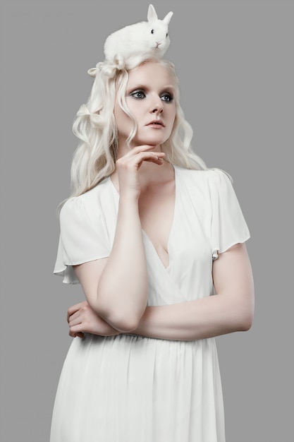 Foto blondes mädchen des albinos im eleganten kleid, das mit nettem kleinem kaninchen aufwirft