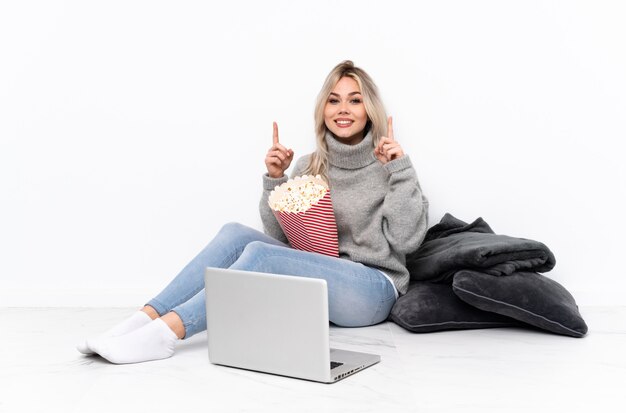 Blondes Mädchen des Jugendlichen, das Popcorn beim Aufpassen eines Films auf dem Laptop zeigt oben eine großartige Idee isst